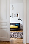 Offene weiße Flügeltür in Altbauwohnung mit durchgehendem Fischgrätparkett, Blick ins Wohnzimmer mit Stehleuchte neben modernem Sofa