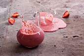 Strawberry smoothies in a glass jug and spilling from a glass