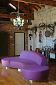 Geschwungenes violettes Designersofa auf Dielenboden unter Glas-Kronleuchter in Loftwohnung mit Industriecharme