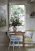 Kitchen chairs at rustic wooden table in corner below window with open white shutters