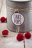 A metal tin of sugar for cake pops with raspberries