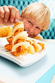 A blonde boy with fruity turkey skewers