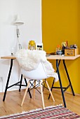 Desk with wooden top on metal frame and sheepskin on shell chair in corner against yellow wall