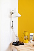 White desk lamp next to yellow storm lamp on wooden table in corner against yellow and white wall