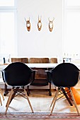 Black shell chairs around white table and retro cinema seats below three hunting trophies on wall