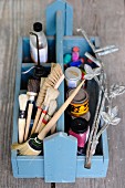 Various paintbrushes, paints and painting utensils in wooden trug