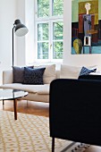 Sessel und Stehleuchte neben weißem Sofa vor Sprossenfenster und modernem Bild