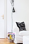 Weisses Hussensofa und Zeitschriftenständer vor Wand mit aufgehängter Arbeitslampe