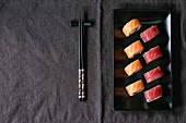Sushi mit Lachs und Thunfisch auf schwarzem Teller, daneben Essstäbchen (Japan)