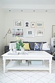White rustic coffee table in front of grey sofa with scatter cushions below gallery of pictures