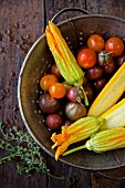 Heirloom tomatoes, yellow courgettes and courgette flowers in a colander