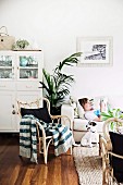 Rattan armchair with knitted blanket and dog in front of sofa with young person lying in living room
