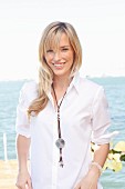 A young blonde woman by the sea wearing a white blouse and jeans