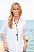 A young blonde woman by the sea wearing a white blouse and jeans