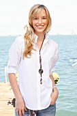 A young blonde woman by the sea wearing a white blouse and jeans