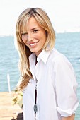 A young blonde woman by the sea wearing a white blouse and jeans