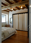 Doppelbett und begehbarer Kleiderschrank hinter Vorhang im Schlafzimmer mit rustikaler Holzbalkendecke