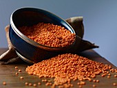 Red lentils in a bowl and in front of it on a wooden table