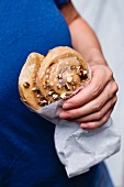 A woman holding a cinnamon and pecan nut bun in a paper bag