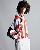 A young woman wearing a horizontally striped jumper holding a handbag