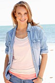 A young woman wearing tops, a denim shirt and jeans on a beach