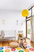 Child on carpet with colorful button pattern and cantilever armchair next to white cot