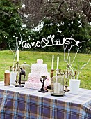 Hochzeitstisch im Garten mit umhäkeltem Schriftzug aus Draht an bemalten Zweigen und einer Hochzeitstorte