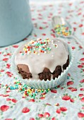 A chocolate muffin with icing and sugar sprinkles