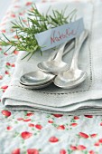 Silver spoons on napkin with name tag and sprig of rosemary