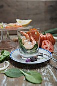 King prawns on a spinach salad in a glass with beefsteak tomatoes, spring onions and lemons in the background