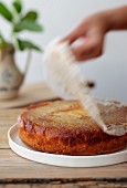 A hand removing parchment paper from an apple cake