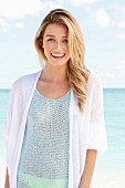 A young woman by the sea wearing a crocheted top and a cardigan