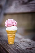 A scoop of coconut and a scoop of strawberry ice cream in an ice cream cone on a wooden table