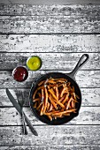 Sweet potato fries in cast iron pan on a rustic wooden surface