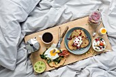 Coffee and various dishes on a wooden board on a white duvet