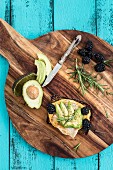 A slice of bread topped with omelette, avocado, blackberries and rosemary