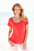 Blonde Frau in rotem Shirt und rosa Hose am Strand