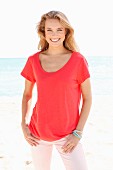 Blonde Frau in rotem Shirt und rosa Hose am Strand