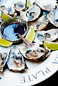 Fresh oysters on a plate with lime wedges and soya and ginger dip