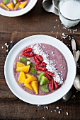 A smoothie bowl with blueberries, banana and apple garnished with raspberries, kiwi, peach and coconut