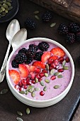 A smoothie bowl with blackberries, blueberries and apple garnished with blackberries, strawberries, pomegranate and pumpkin seeds
