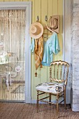 Gilt chair below coat rack on yellow wall