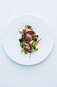 Wild rabbit wrapped in bacon on a mixed leaf salad with blackberries