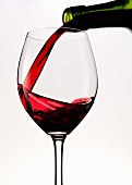 Rotwein in ein Rotweinglas gießen
