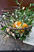 Sprigs of mistletoe and tangerine in metal basket (festive)