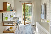 Washstand with wooden base unit and open glass door with garden view in bright modern bathroom