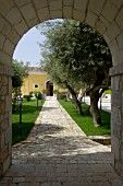 Blick durch mediterranen Torbogen auf gepflasterten Weg durch den Garten
