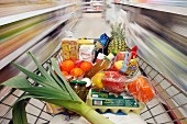 Einkaufswagen voller Lebensmittel zwischen Regalen in Supermarkt
