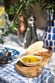 Holzbrett mit Brot, Öl und Oliven auf mediterran gedecktem Tisch