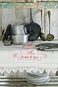 Rustikaler Holzschrank mit Vintage Geschirr und weißem Tischtuch mit Spitzenbordüre und Stickerei